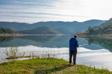 Back view of man fishing on the lake in the morning with beautiful landscape in the background
