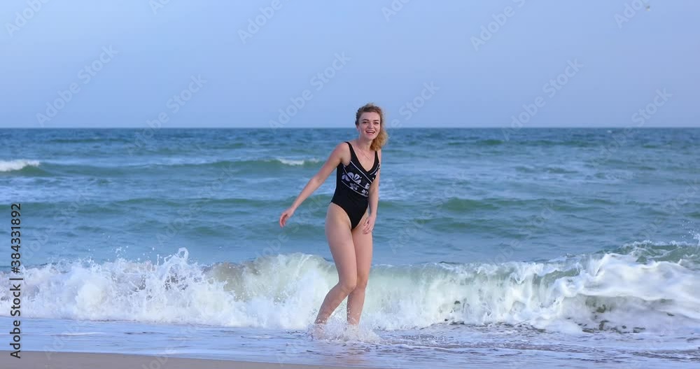 Happy curly woman in black swimsuit runs on the waves enjoying in the splashes Happy curly woman in black swimsuit runs on the waves enjoying in the splashes