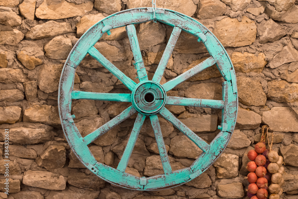 a cart wheel hangs on a stone wall.