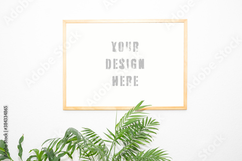 real wood picture frame mockup on a white wall with plants projecting into the picture from below, real photo as design template photo