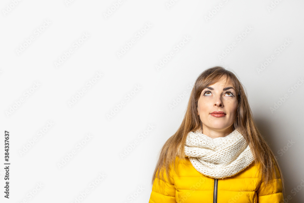 Woman in a jacket and scarf looks up on a white background. Concept dream, planning, pensive, surprise Woman in a jacket and scarf looks up on a white background. Concept dream, planning, pensive, surprise
