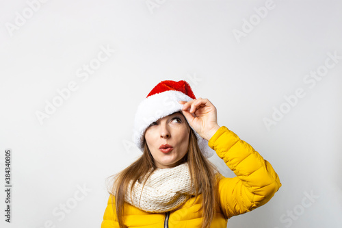 Young woman looks out from under Santa Claus hats wearing eyes on a light background. Concept of winter  winter holidays  Christmas  New Year. Funny mood  emotions  surprise  shock