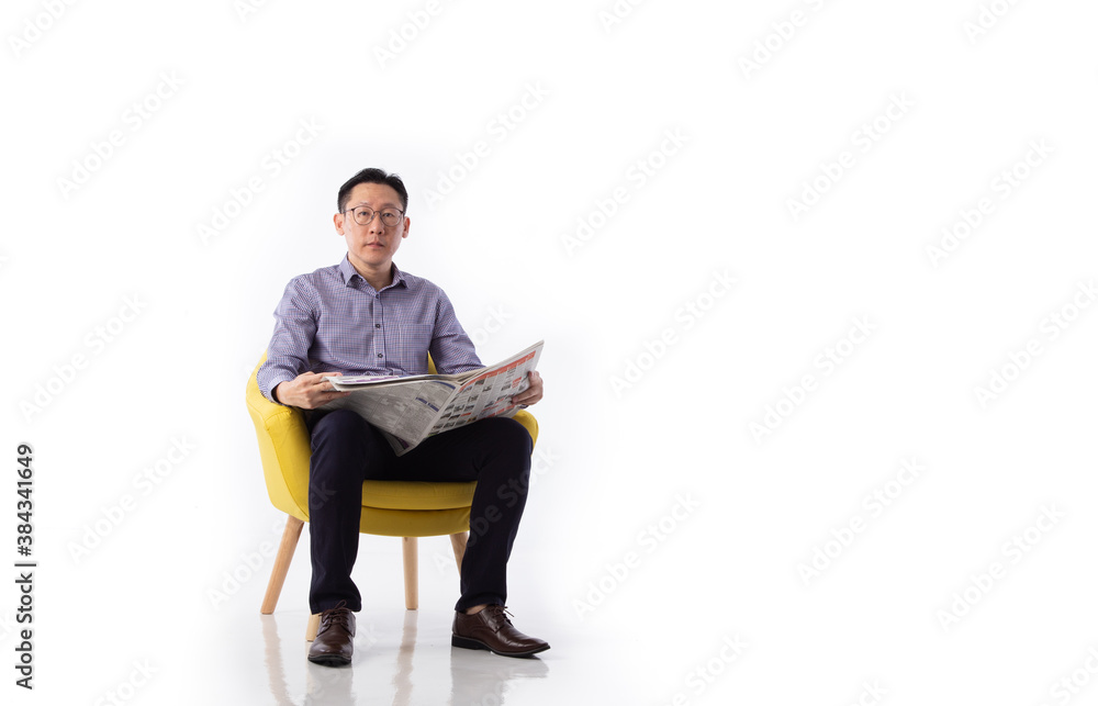 An Asian man seated in an armchair reading a newspaper. An Asian man seated in an armchair reading a newspaper.