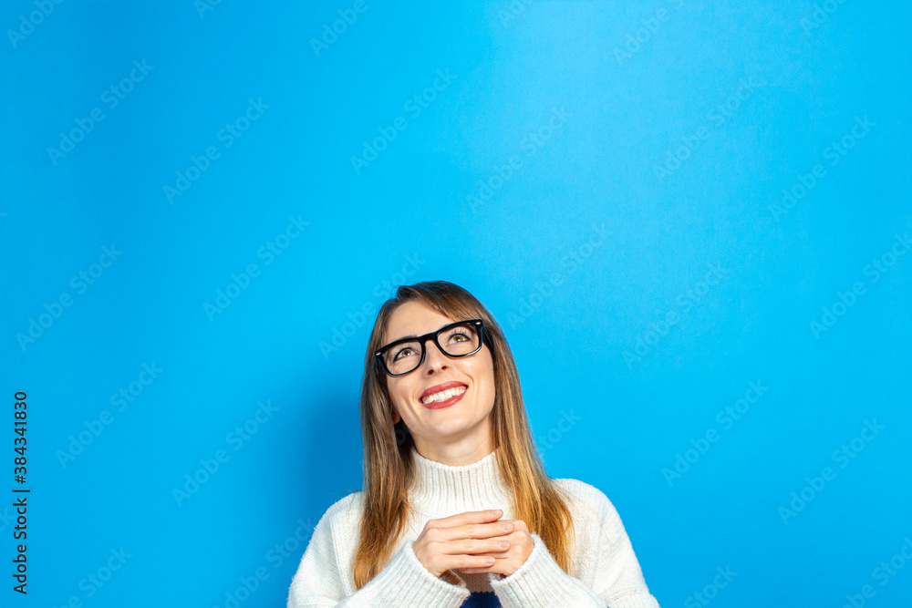 young girl with glasses and in a knitted sweater looks up, smiles, happy, dreams, ideas arose on a blue background. Banner