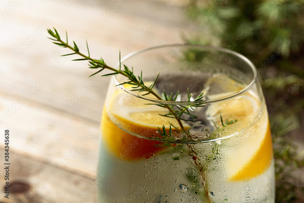 Alcohol drink (gin tonic cocktail) with lemon, juniper branch, and ice on rustic wooden table. - obrazy, fototapety, plakaty 