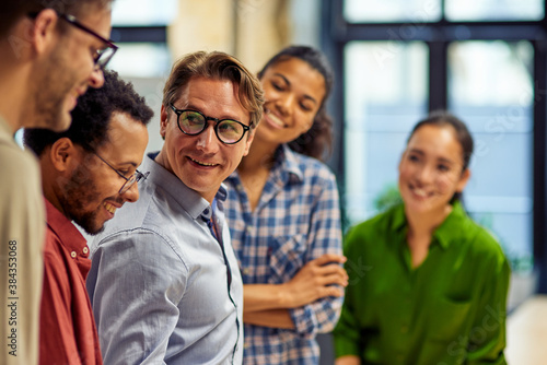 Confident businessman discussing project results and sharing ideas with young motivated multi ethnic team while standing together in the modern office