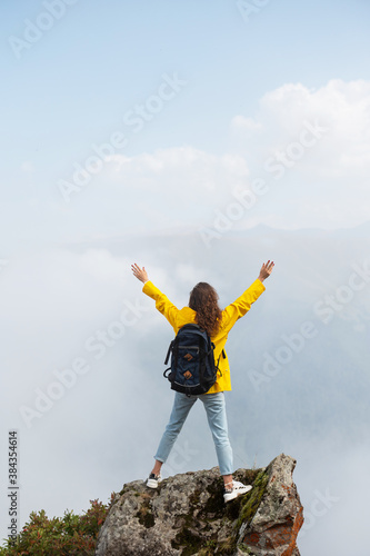 Young happy woman rising hands on the top on the mountain against clouds on the background