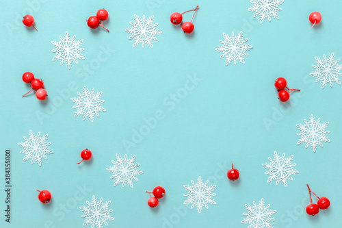 Xmas decoration. Red berry, white snowflakes in shape frame on pastel blue background for greeting card. Copy space. Winter holidays, New Year.