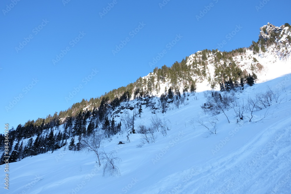 Winter mountain landscape at Baikal. Khamar-Daban ridge. Snow-capped peaks, chalets in the mountains. Winter forest.