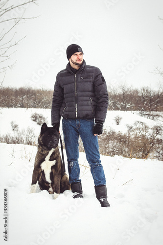 A man in a jacket and a knitted hat walks with an American Akita dog