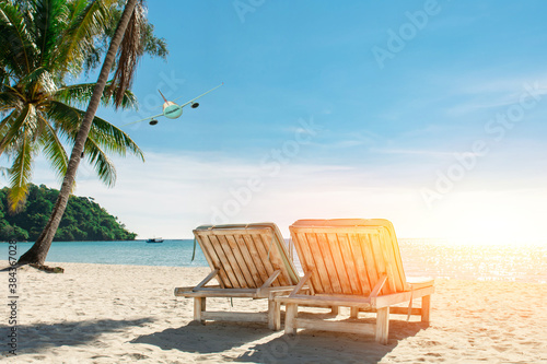 Wooden beach chairs and parasols on tropical sandy beach in the morning with white passenger airplane landing above the sea , destinations relax summer holidays concept