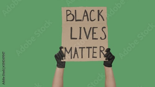 Female hands in black gloves pick up a poster from a cardboard box that reads BLACK LIVES MATTER. Struggle for equality and unity. Isolated a green screen, chroma key. Close up. Slow motion. photo