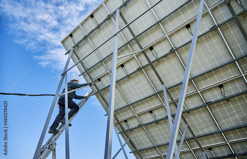 Horizontal snapshot of solar module ground mounting maintaining solar batteries and worker on ladder installing panels. Low angle view. Concept of renewable resources Horizontal snapshot of solar module ground mounting maintaining solar batteries and worker on ladder installing panels. Low angle view. Concept of renewable resources