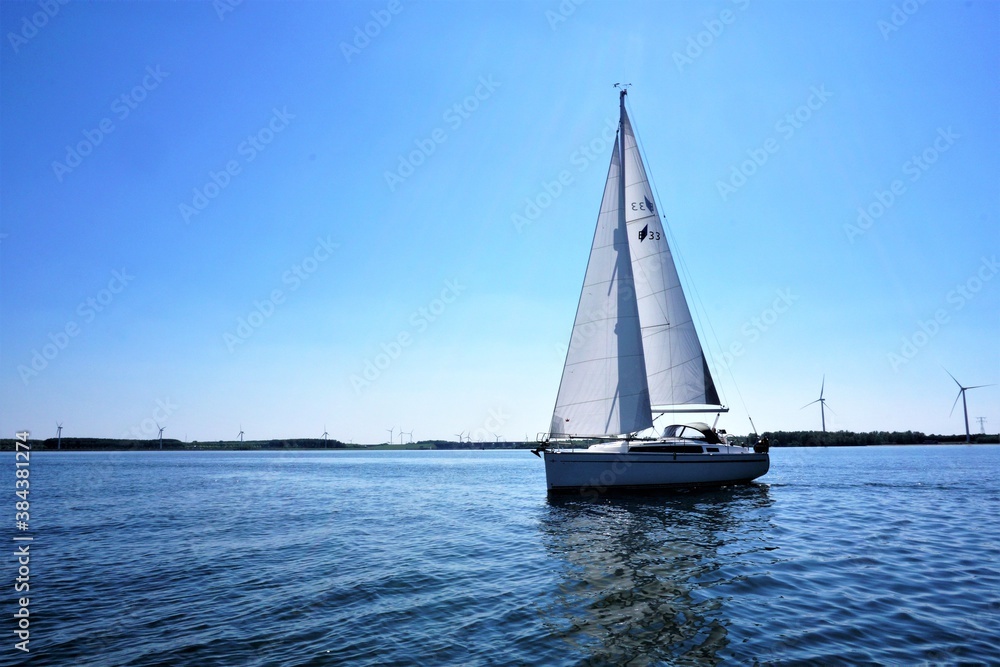 Sailboat on calm waters, isolated with windmills in the background. Optimal green energy.