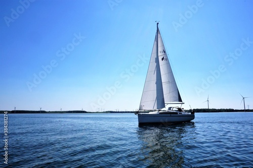 Sailboat on calm waters, isolated with windmills in the background. Optimal green energy.