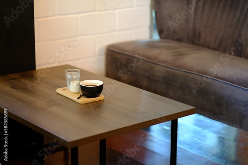 Black coffee cup with water and sugar placed on a wooden table.