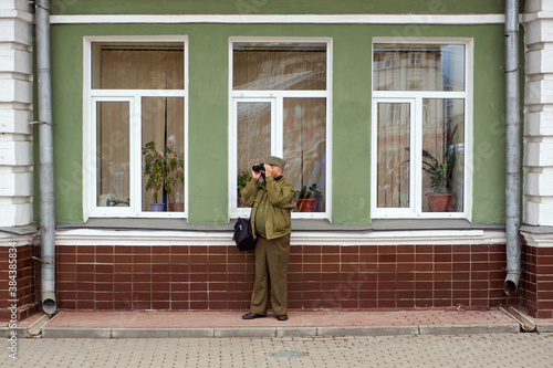 A man stands against the wall and looks through binoculars