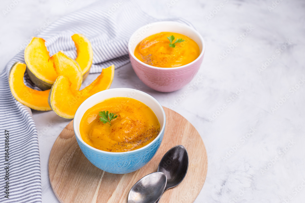 Delicious pumpkin soup in bright bowls on a light background. Copy space. Close-up, horizontal. Vegetarian delicious food. Delicious pumpkin soup in bright bowls on a light background. Copy space. Close-up, horizontal. Vegetarian delicious food.