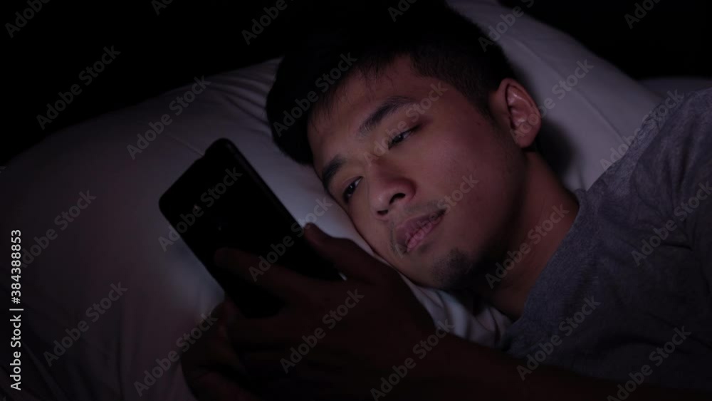 Young Asian man using a smartphone in his bed at night Young Asian man using a smartphone in his bed at night