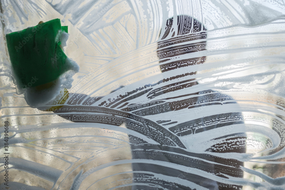 The man behind the window glass washes off the soap suds with a rag and water. washing Windows