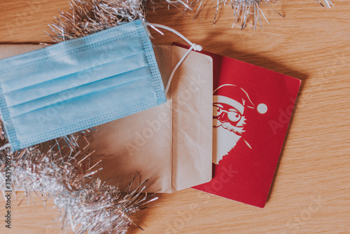 Tarjeta de navidad en su sobre marrón con una mascarilla quirúrgica para el Covid-19 y un espumillón photo