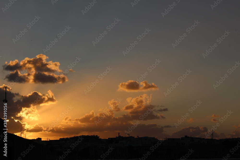 A photograph of a vibrant sunset with sunlight rays filtering out from beautiful fluffy clouds, with copy space