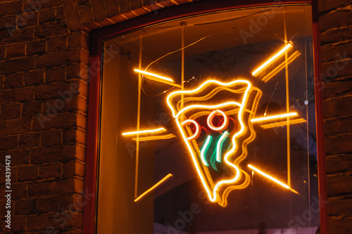 Neon sign slice of pizza on the window of the pizzeria at night glows advertisement