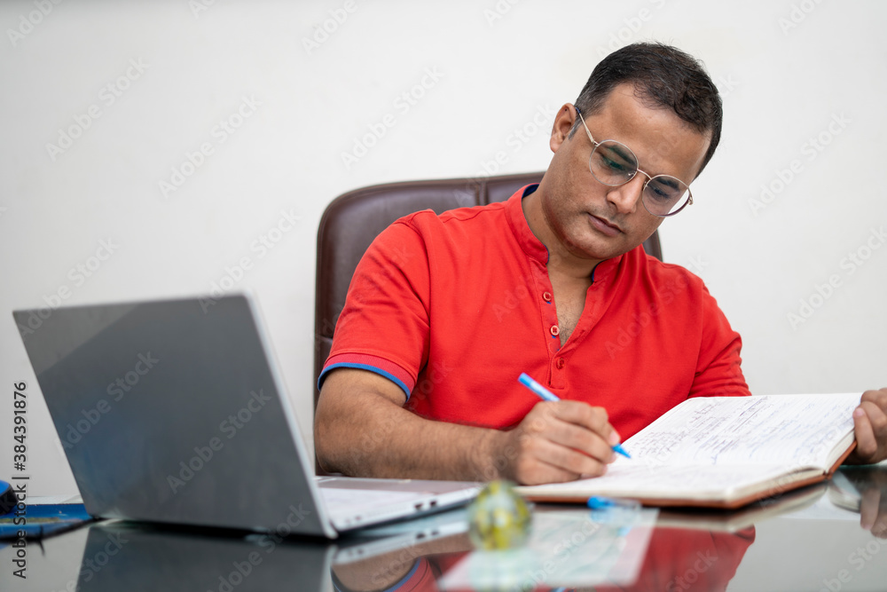 technology, remote job and lifestyle concept - happy indian man in glasses with laptop computer working at office. technology, remote job and lifestyle concept - happy indian man in glasses with laptop computer working at office.
