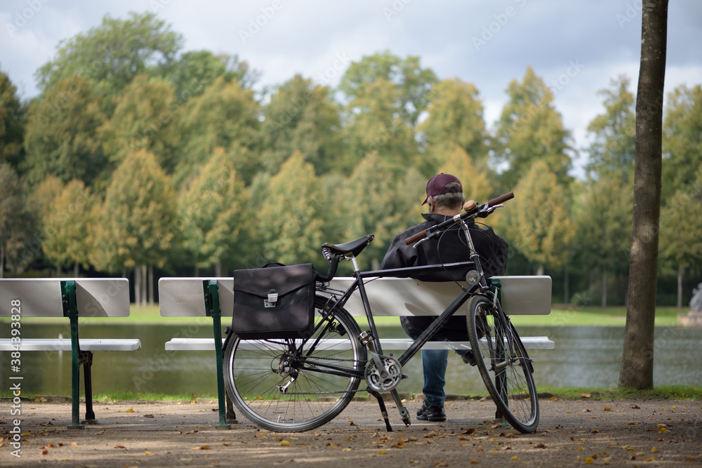 Man enjoys sun on park bench with bicycle. Everyday life during corona quarantine.