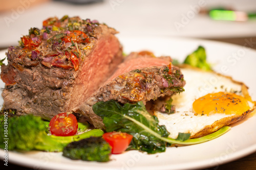 Roasted and seasoned meat with accompaniment of fried egg, brocolis, onion and tomato.