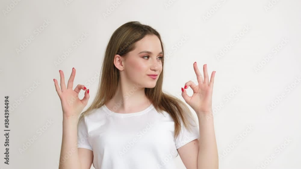 OK gesture. Agreement sign. Portrait of amused teen girl in white t-shirt showing deal signal smiling with braces isolated on light background. Good idea. Yes answer. OK gesture. Agreement sign. Portrait of amused teen girl in white t-shirt showing deal signal smiling with braces isolated on light background. Good idea. Yes answer.