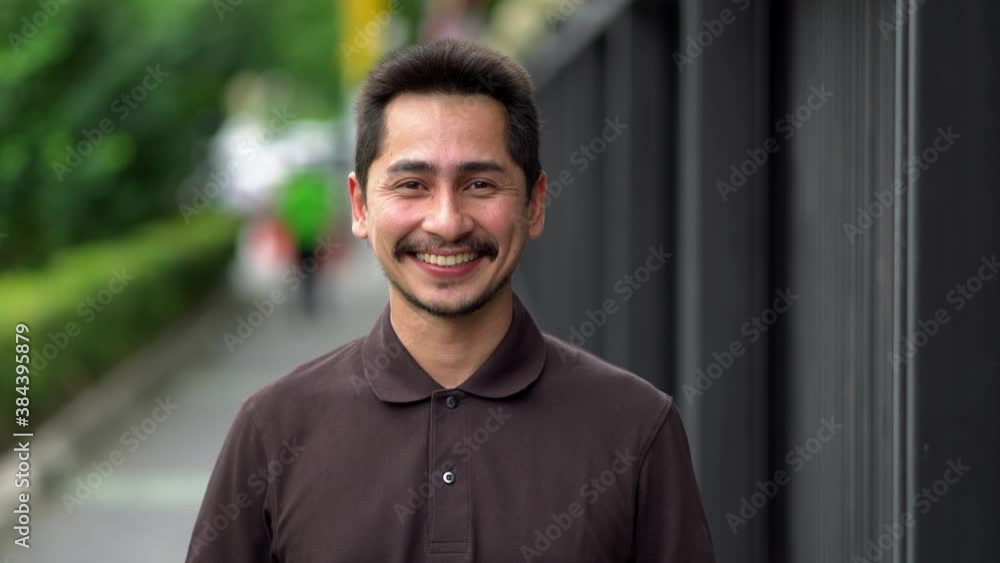 Young man asian smiling and looking at camera. Portrait of a happy handsome young man in a urban street. Close up face of young cool trendy man looking at camera Young man asian smiling and looking at camera. Portrait of a happy handsome young man in a urban street. Close up face of young cool trendy man looking at camera