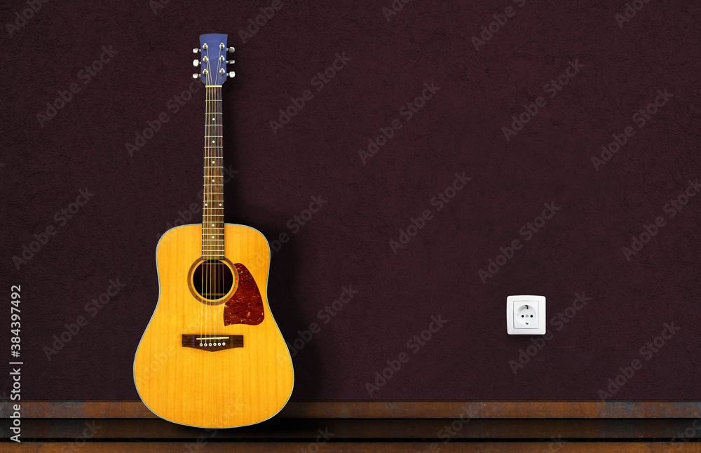 Fototapeta premium Acoustic guitar resting against a dark wall