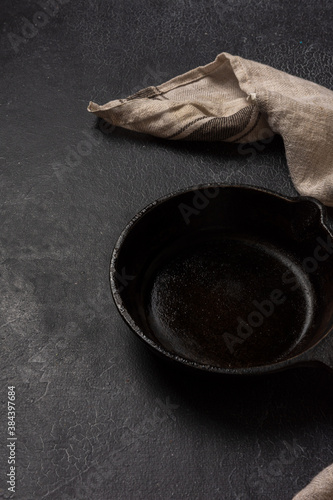 Empty black cast iron frying pan on a dark graphite background. Light linen towel.