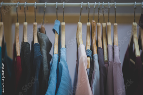 Stylish clothes in dark colors hang on wooden hangers in a store or wardrobe. Rack with women's and men's clothing. Coloring and toning