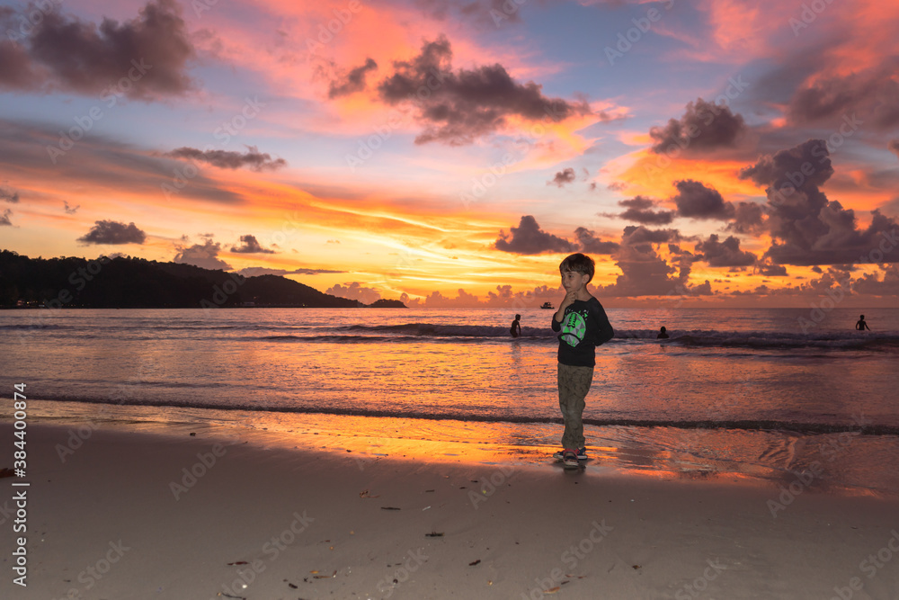 .A cute boy standing on Patong beach during stunning sunset