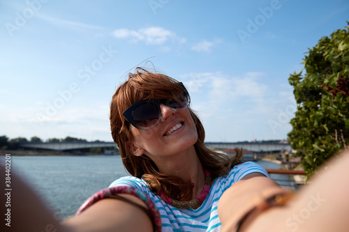 Young woman taking selfie outdoors near the river in city environment.
