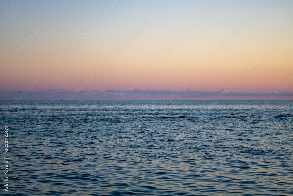 Beautiful panoramic view of the sunset over the Sochi sea with dark pink clouds and a view of the pebble beach.