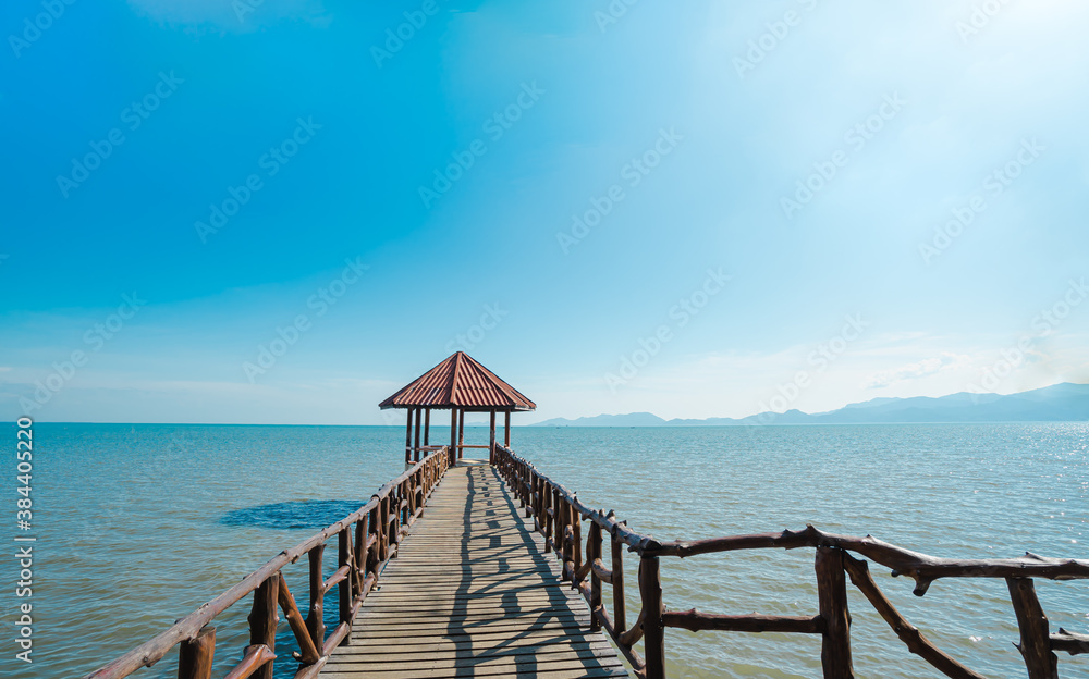 Front view of the iron pavilion in the sea. There is wooden bridge into the blue ocean in the morning with sky is bright blue and white clouds. The idea for cold background and copy space on the top.