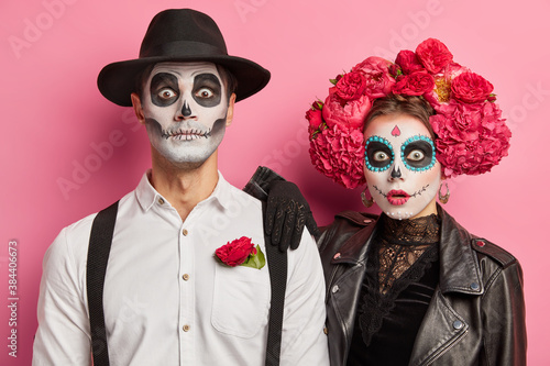 Mexican woman and man pose surprised in costumes as see something terrible celebrate day of dead traditional Mexico holiday have image of zombies pose against pink background. Happy Halloween concept