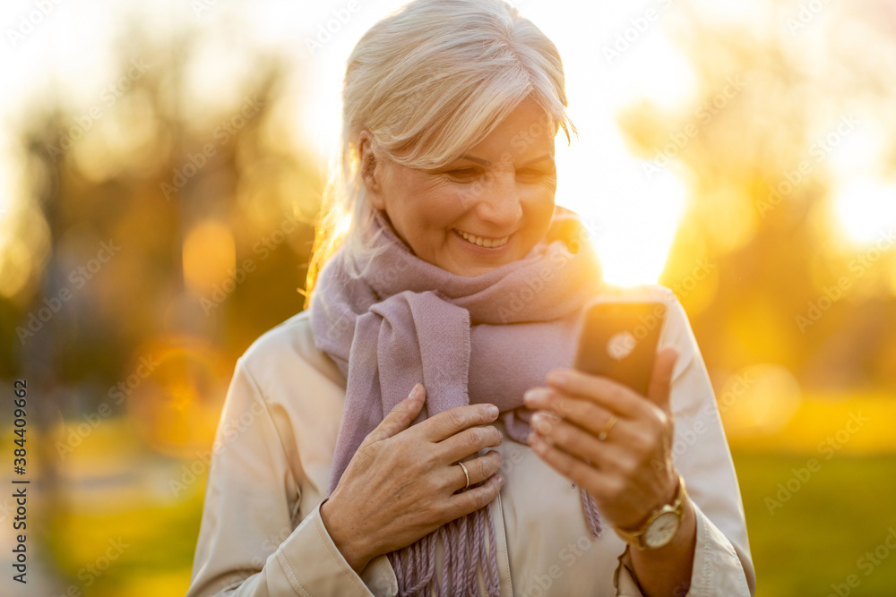 Senior woman using mobile phone outdoors at sunset
 - obrazy, fototapety, plakaty 