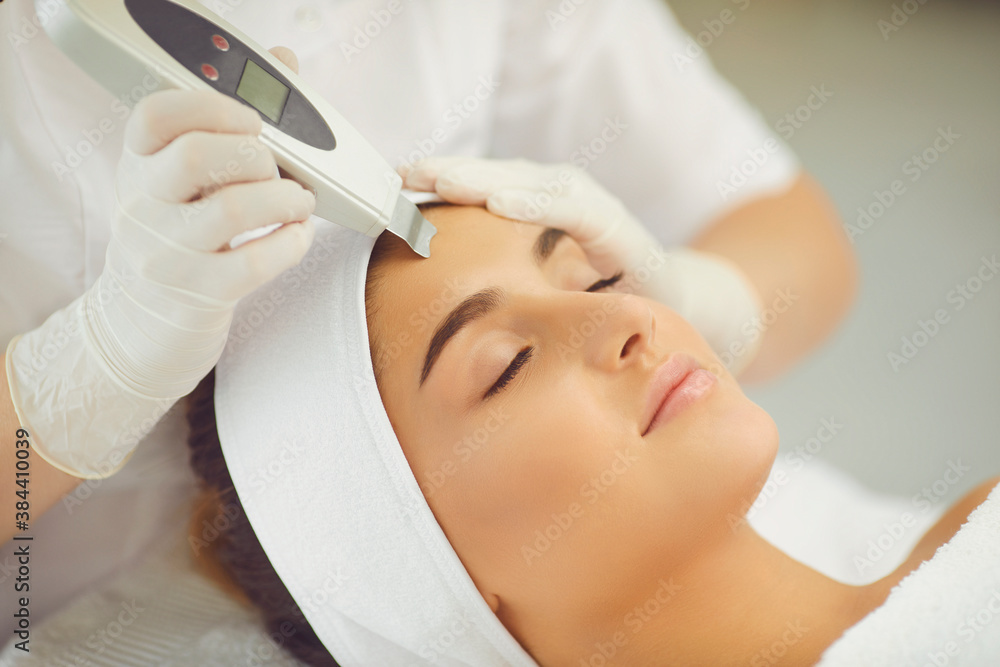 Naklejka premium Relaxed woman getting ultrasound apparatus facial cleaning from cosmetologist