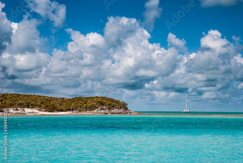 Wide open view of tropical turquoise ocean waters in the caribbean bahamas with one island and single sailboat paradise isolation