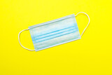 Blue medical mask on bright yellow background. Stop respiratory epidemic concept.