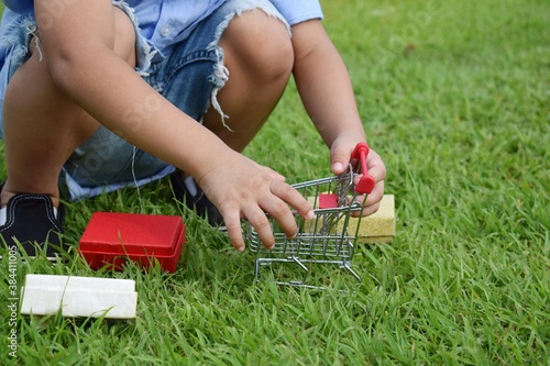 The hand of a boy playing a small cart with a small box in the lawn.