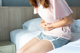 Unhealthy young woman sitting on bed and holding belly, feeling discomfort and suffering from stomachache, food poisoning, on period. Health problem concept