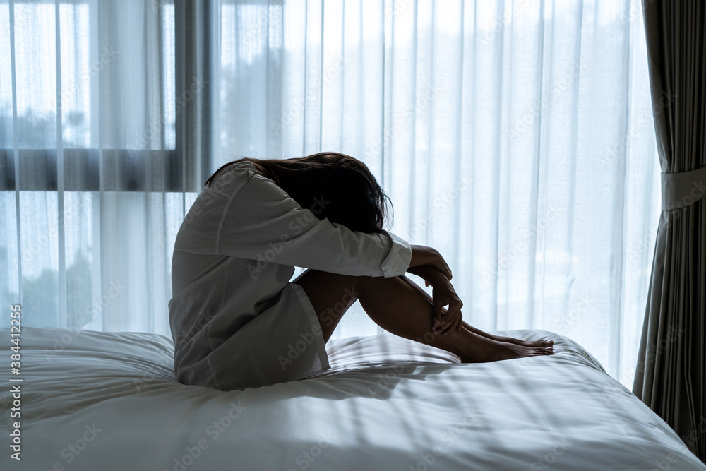 Stressed young Asian woman suffering on depression and sitting alone in dark bedroom at home. sad, unhappy, disappointed concept