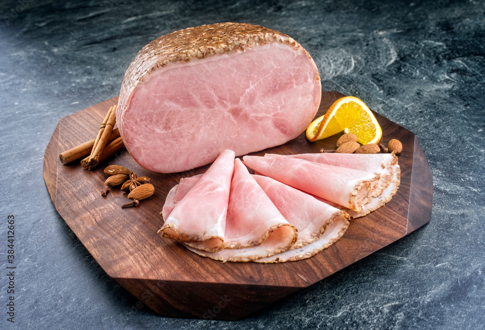 Traditional German boiled Christmas ham with almond, cinnamon and orange offered as close-up on a modern design wooden board with copy space