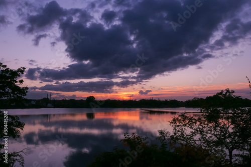 Amazing sunrise in rural scene. Symmetry of the sky in a lake at sunset. Clouds reflecting on the water. Quiet relaxing scene with a beautiful colorful cumulonimbus. Silhouette of vegetations.