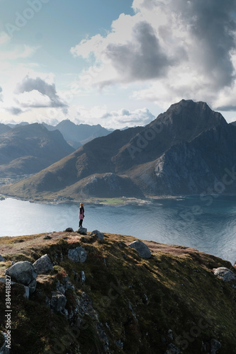 Young woman is standing at the top of mountain and enjoying view over amazing landscape on Lofoten Islands. She stick to social distancing. No tourist in Covid-19 pandemic times.